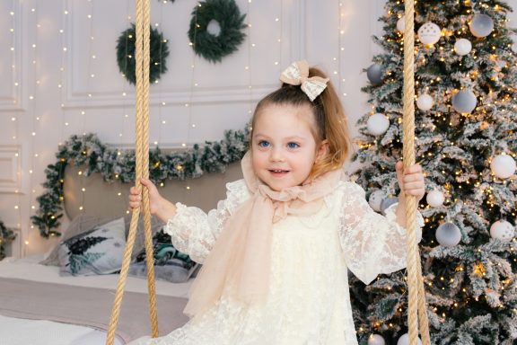 Navidad 2025 Niña sentada en columpio navideño, en una habitación decorada para navidad