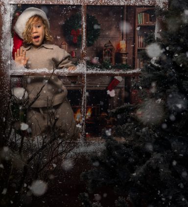 Navidad 2024 Niño con gorro de Santa mirando por la ventana en un ambiente navideño.