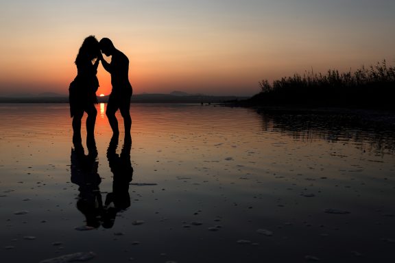 Siluetas de una pareja abrazándose al atardecer en una playa tranquila.