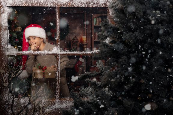 Navidad 2024 Persona con gorro de Navidad mirando por la ventana mientras nieva.