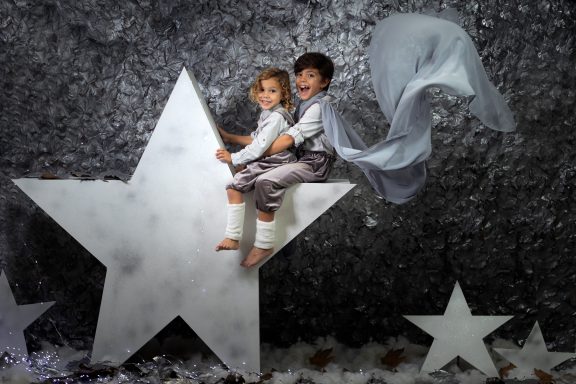 Navidad 2023 Dos niños sentados sobre una gran estrella, uno con capa y ambos sonrientes.