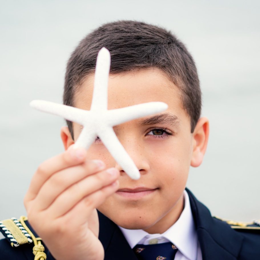 Niño vestido de comunión sostiene una estrella de mar blanca frente a él.
