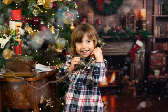 Navidad 2024 Niña sonriente con un teléfono antiguo, decoraciones navideñas y una chimenea de fondo.