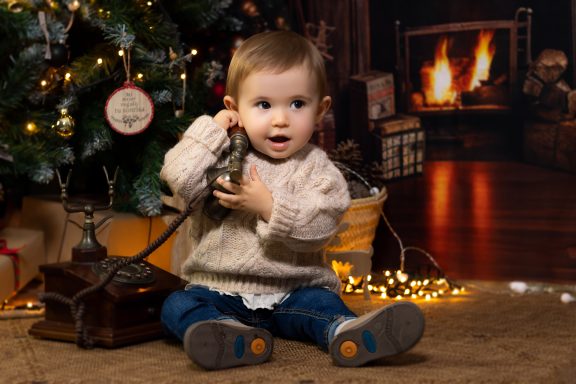 Navidad 2024 Niño pequeño sentado junto a un árbol de Navidad, hablando por un teléfono antiguo.