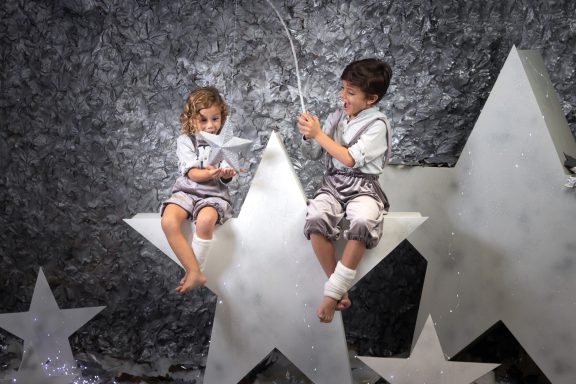 Navidad 2023 Niños sentados en estrellas grandes de papel, uno juega con un hilo brillante.