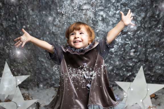 Navidad 2023 Niño feliz con los brazos levantados, vestido con un abrigo y rodeado de estrellas plateadas.