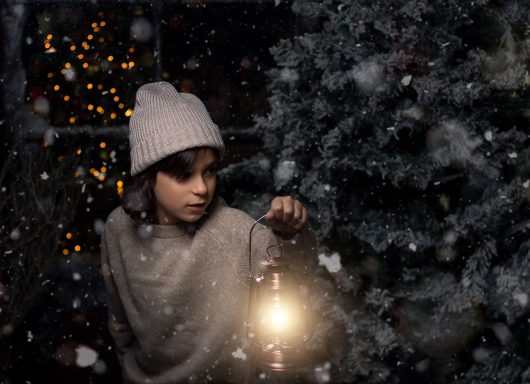 Navidad 2024 Niño con gorro y abrigo, sosteniendo una linterna junto a un árbol de Navidad. Nieve cayendo.