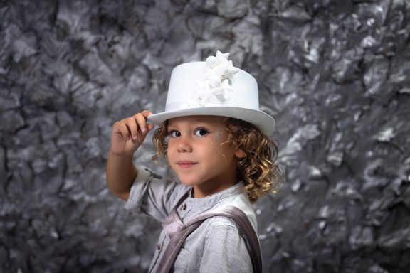 Navidad 2023 Niño con cabello rizado, usando un sombrero blanco y sonriendo, vestido con camisa clara.