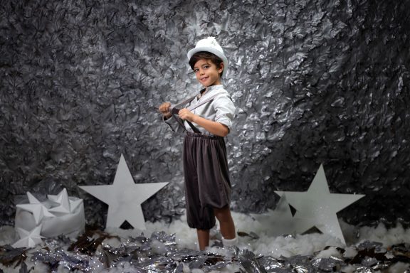 Navidad 2023 Niño con gorra y tirantes, posando entre estrellas en un fondo plateado.